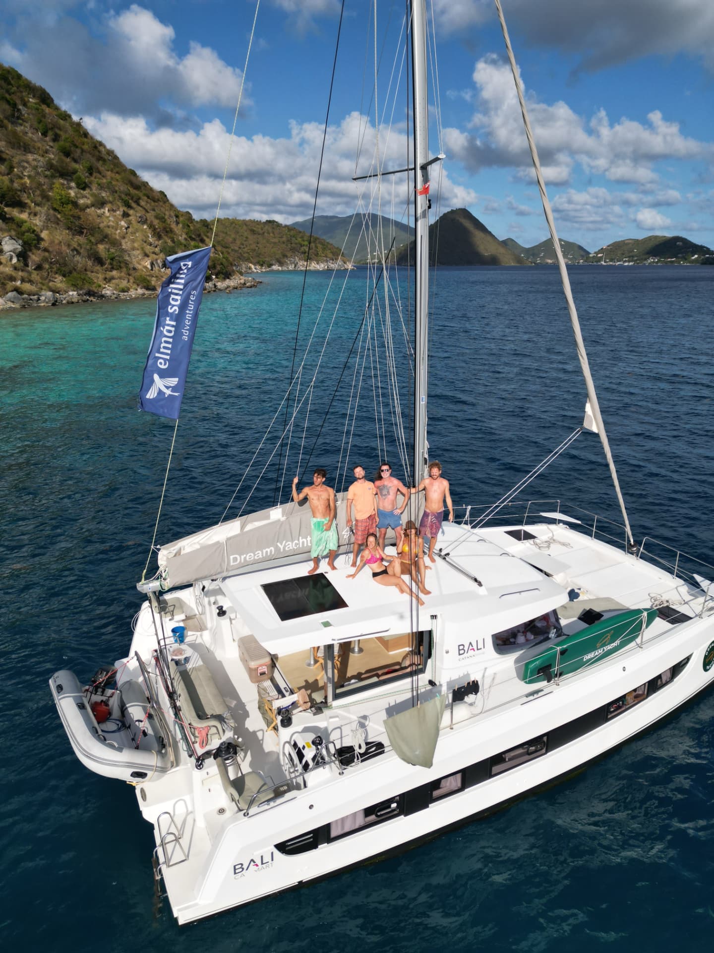 Group of travellers relaxing on the upper deck of a sailing catamaran with green islands behind