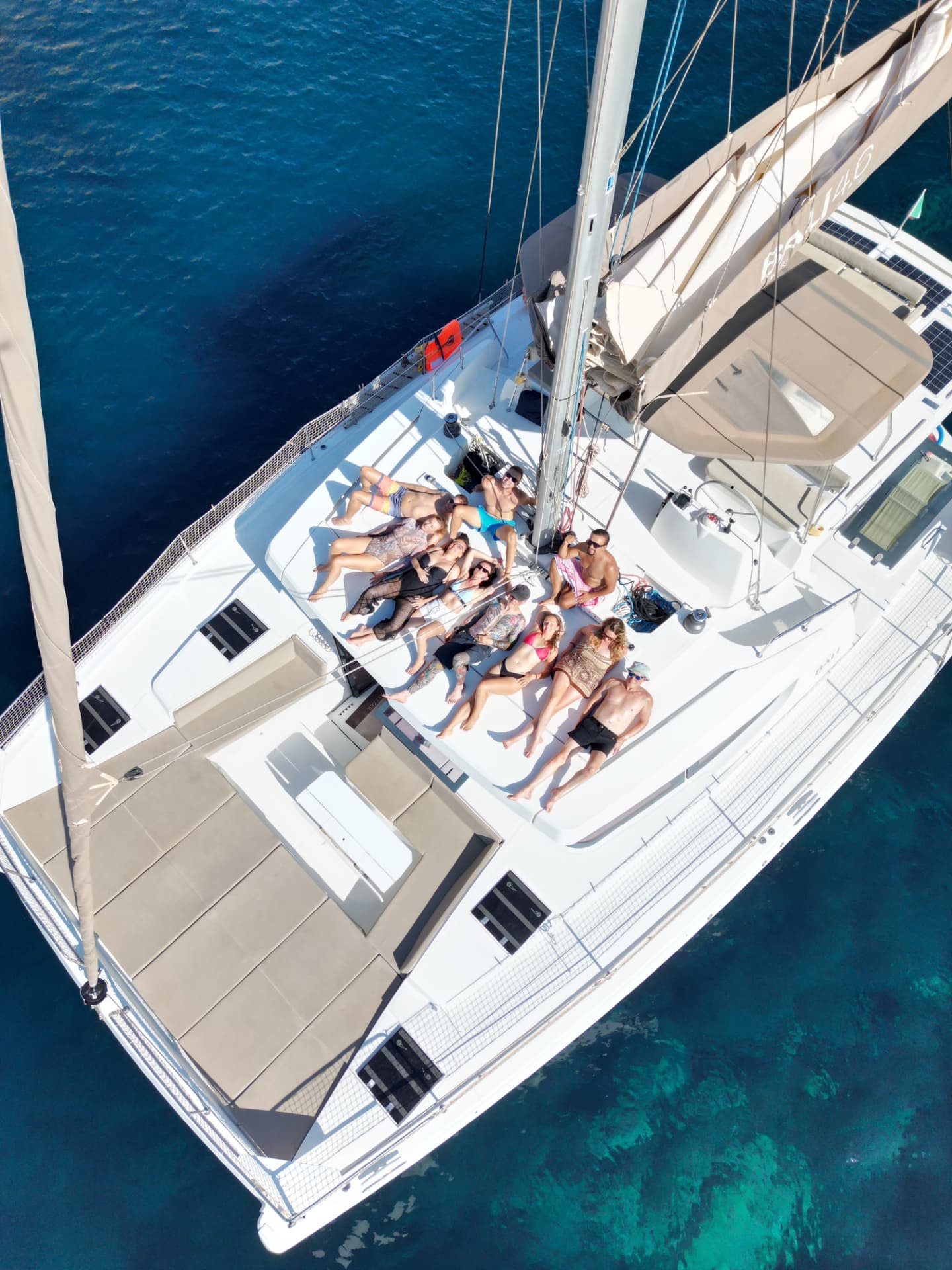 Aerial view of the crew relaxing on the sun deck of a catamaran anchored in turquoise water