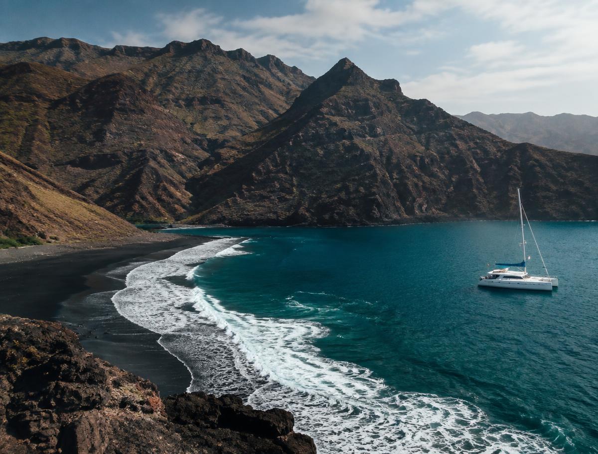 Black sand volcanic cove in the Canary Islands with a catamaran offshore