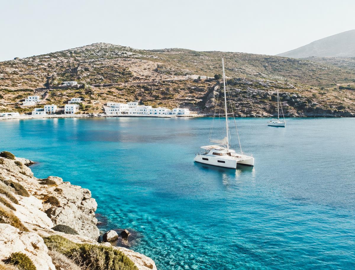 Catamaran anchored in a turquoise Greek bay with whitewashed houses